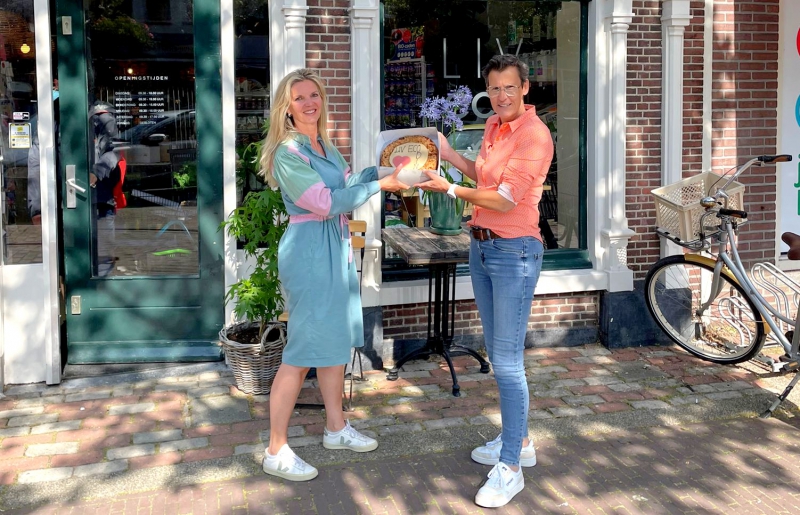 Petra Rustenburg (links, Liv Eco) en Merle Koomans van den Dries (rechts, Odin) vieren de overdracht van biologische winkel Liv Eco in Medemblik aan Odin met een taart 