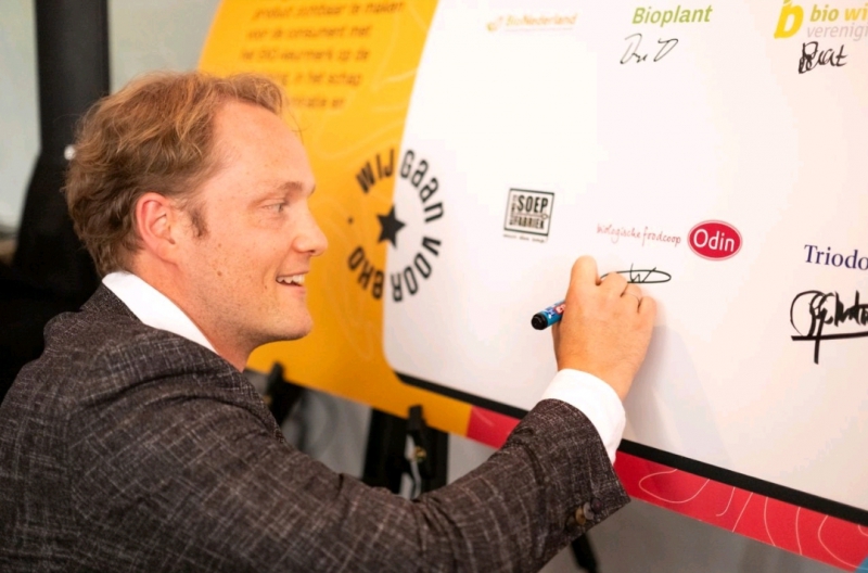 Man ondertekent EKO-NL Ketenconvenant-document, vertegenwoordigend duurzame landbouw van Foodcoop Odin, met logo’s van Triodos en Wij kunnen Beter Boeren.